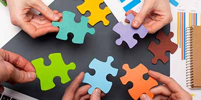 Múltiplas mãos trabalhando em conjunto para montar um quebra-cabeça colorido, simbolizando a colaboração, o trabalho em equipe e a busca por soluções integradas que a Alternativa Sistemas oferece para os desafios de ERP em e-commerce multiempresa.